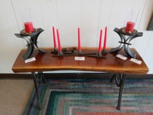 Table made of wood with metal legs with three metal candle holders with red candles inside by blacksmith Nathan Olinger