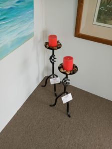 Tall metal candle holders with red candles and stones around the top by blacksmith Nathan Olinger